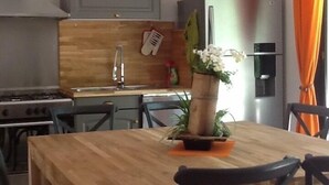 Une cuisine moderne avec une table en bois, des chaises, un porte-ustensiles suspendu et un réfrigérateur en acier inoxydable.
