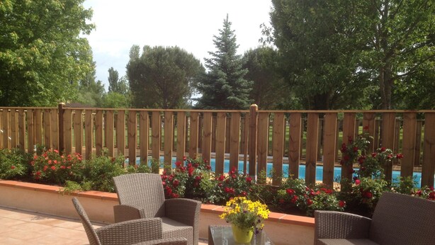 Une terrasse extérieure aménagée avec des meubles en osier, une table en verre et une vue sur une piscine et un jardin.