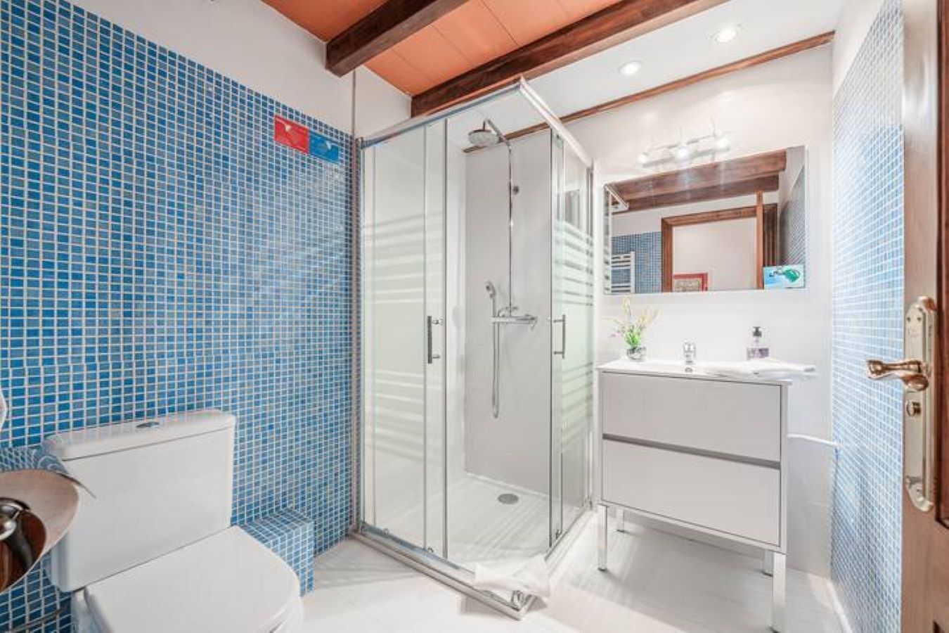 A bathroom with a glass shower enclosure, a white sink, and a toilet.