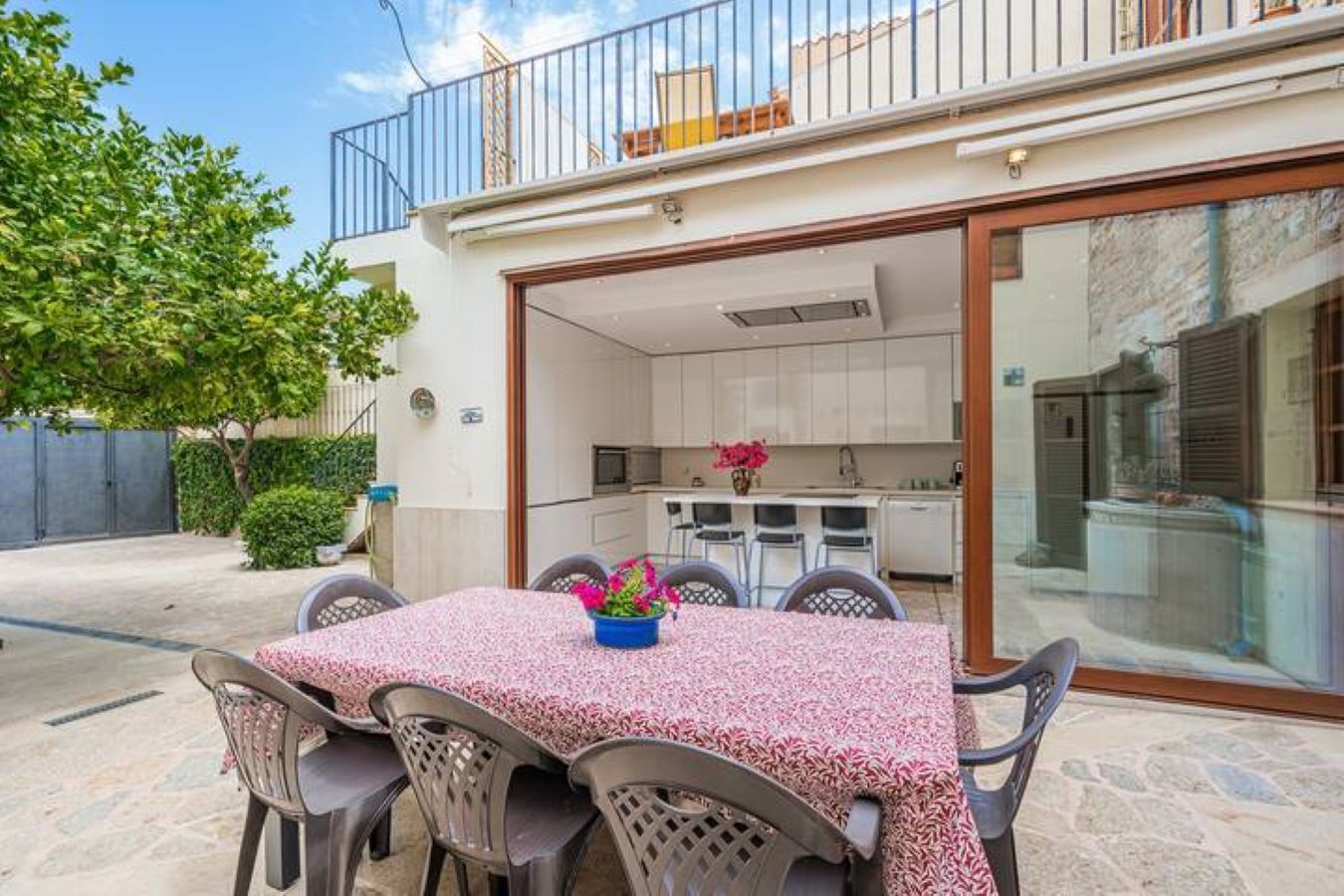 Une terrasse avec une table et des chaises, une petite cuisine visible à travers une porte ouverte, et un balcon avec une balustrade.