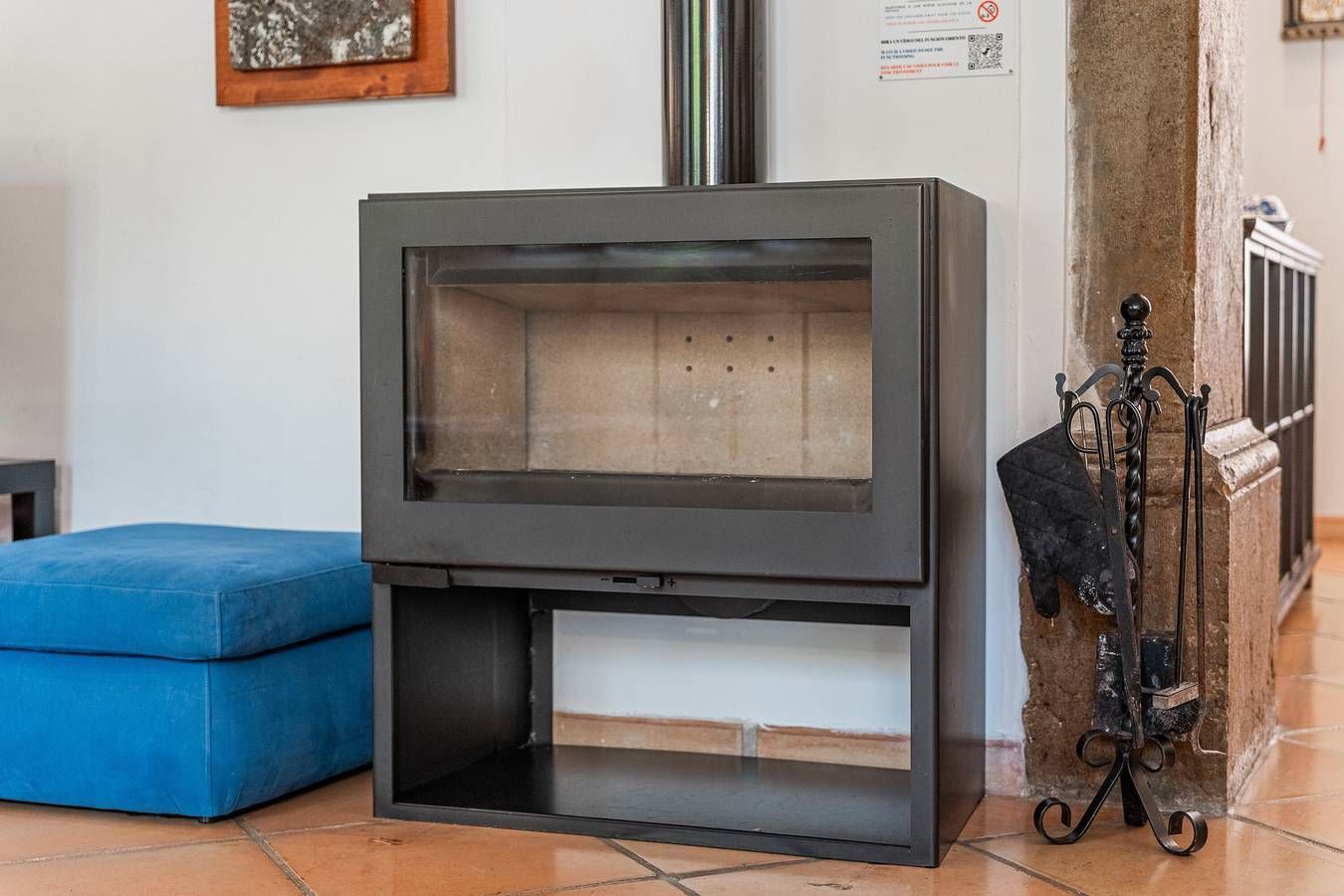 Een moderne haard met een glazen voorpaneel, een blauwe bank en een metalen standaard met een jas.