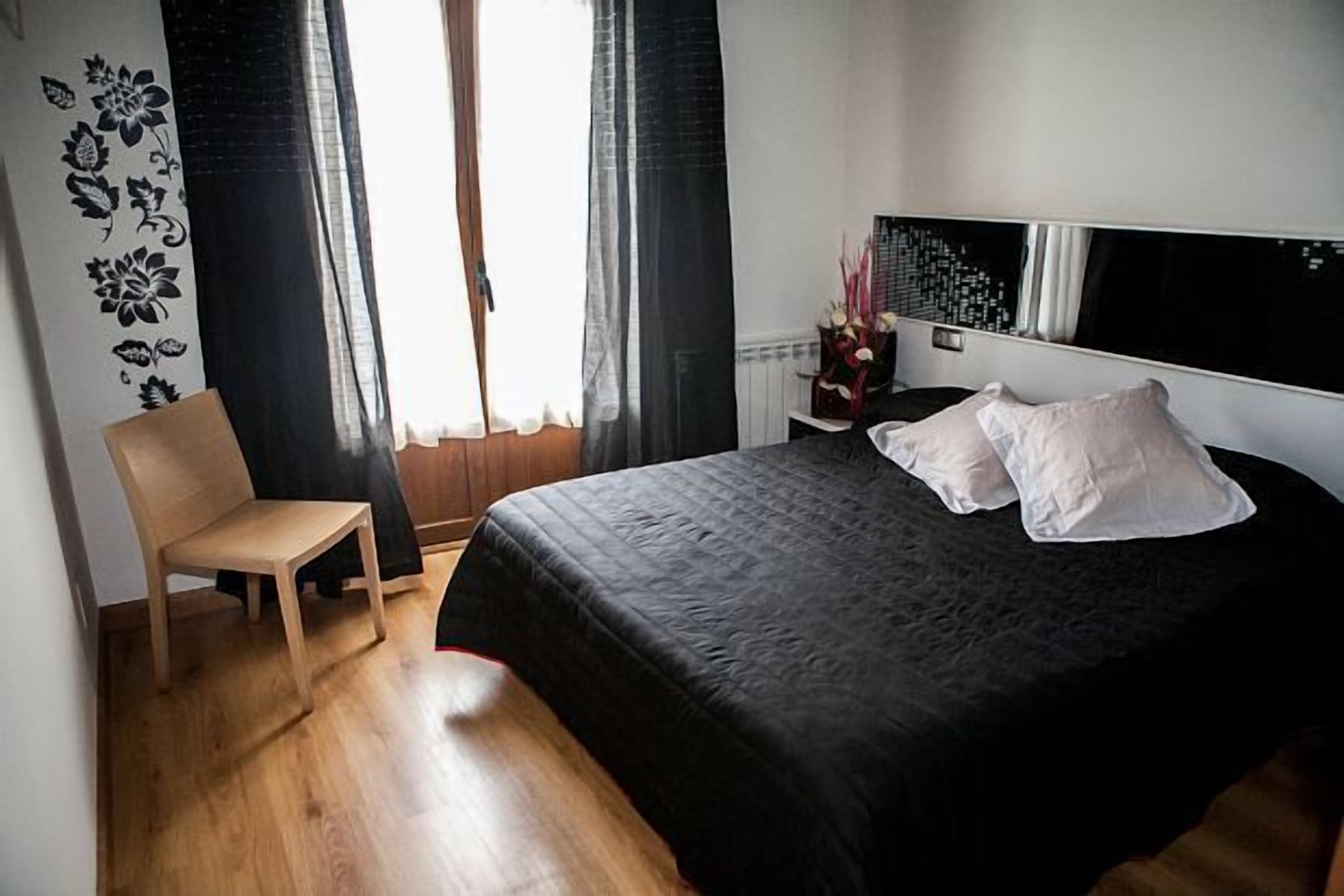 A bedroom with a bed, a chair, a nightstand, and a wall with a floral design.