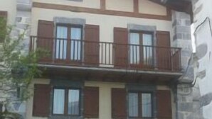 Un edificio de dos pisos con fachada de piedra, un balcón en el nivel superior y un garaje en la parte frontal.
