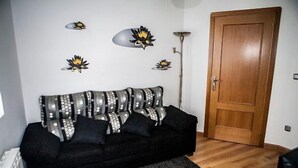 Una sala de estar con un sofá negro, decoración en la pared, una puerta de madera y una lámpara de pie.