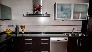 Una cocina moderna con armarios oscuros, lavavajillas de acero inoxidable, horno empotrado y microondas.