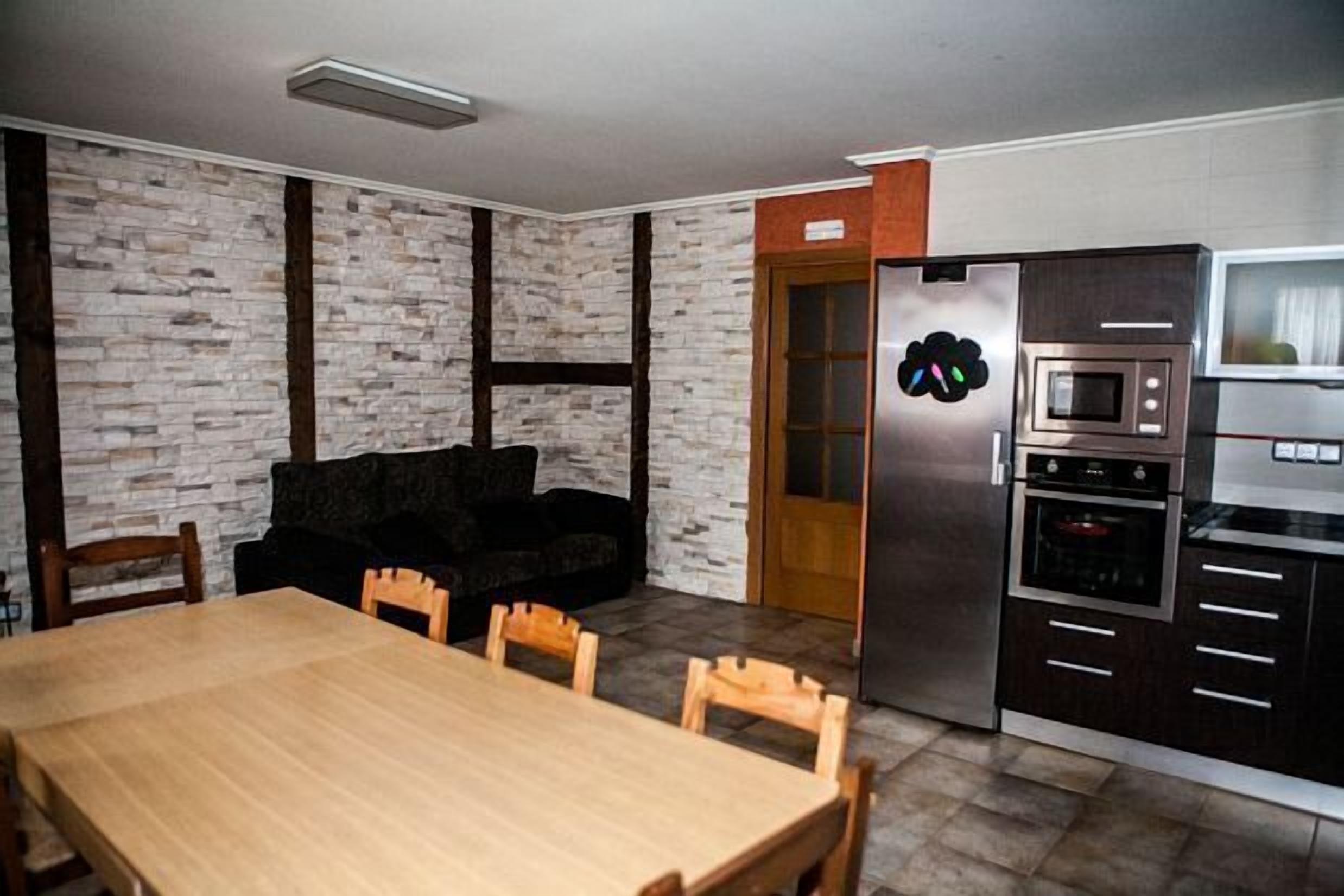 Una cocina moderna con horno empotrado, microondas y refrigerador. Hay una mesa de comedor con sillas y un sofá negro.