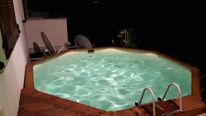 Ein sechseckiger Whirlpool mit Holzterrasse, umgeben von einer weißen Wand und einem Fenster.