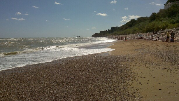 Ein kiesiger Strand mit Wellen, einem klaren Himmel und felsigen Klippen.