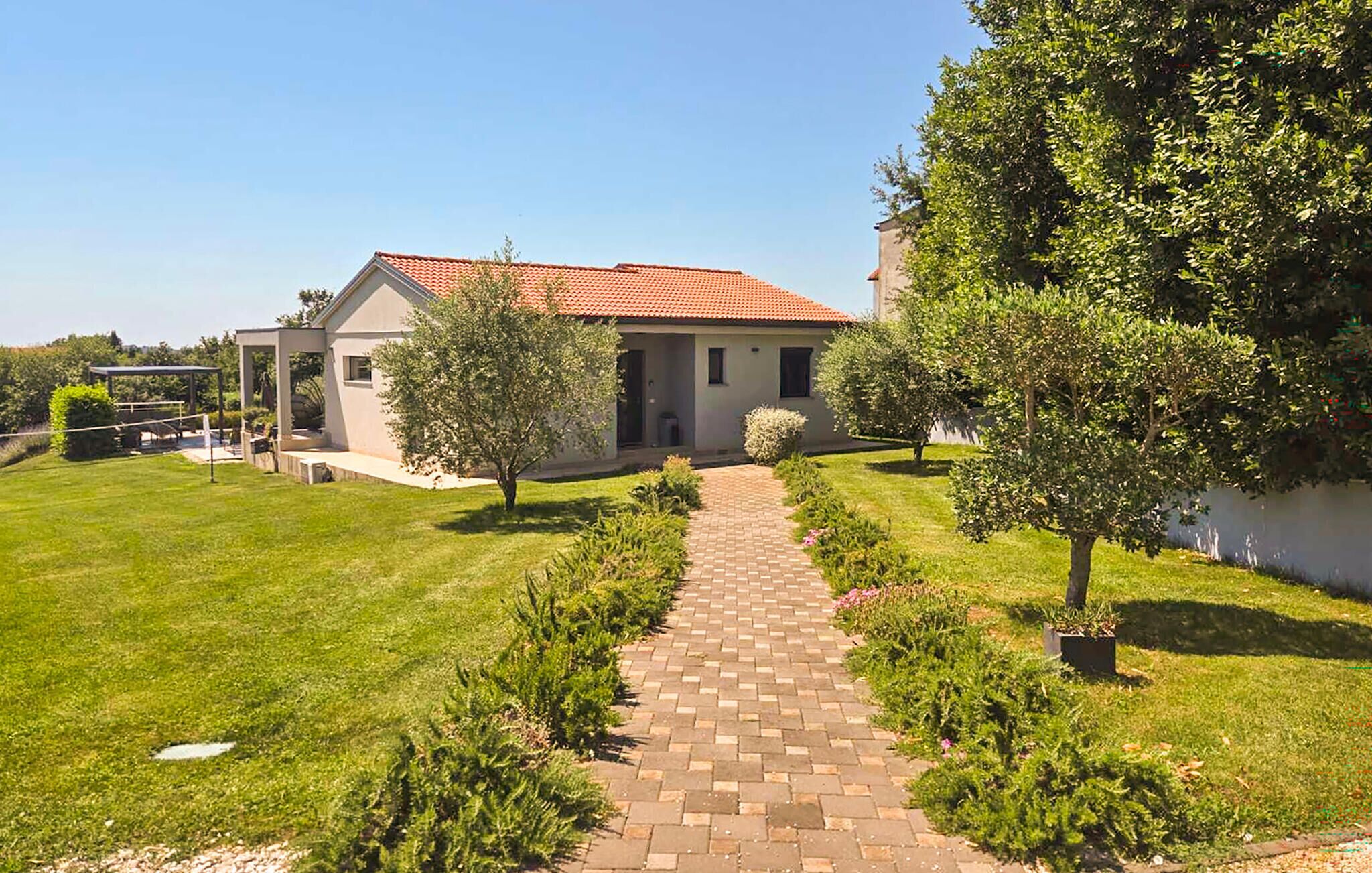 A house with a paved pathway leading to the entrance, surrounded by well-maintained grass and trees.