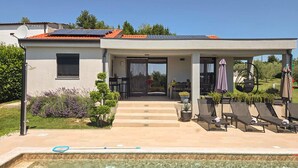 Une maison moderne dotée d’une piscine, d’un patio couvert avec des chaises longues et de panneaux solaires sur le toit.