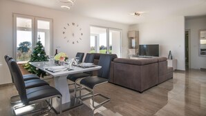 Un salon moderne avec un coin repas, comprenant un canapé, des fauteuils, un téléviseur et un sapin de Noël.