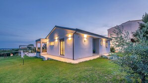 Une maison moderne à deux étages, dotée d’un patio couvert et d’une pelouse bien entretenue.