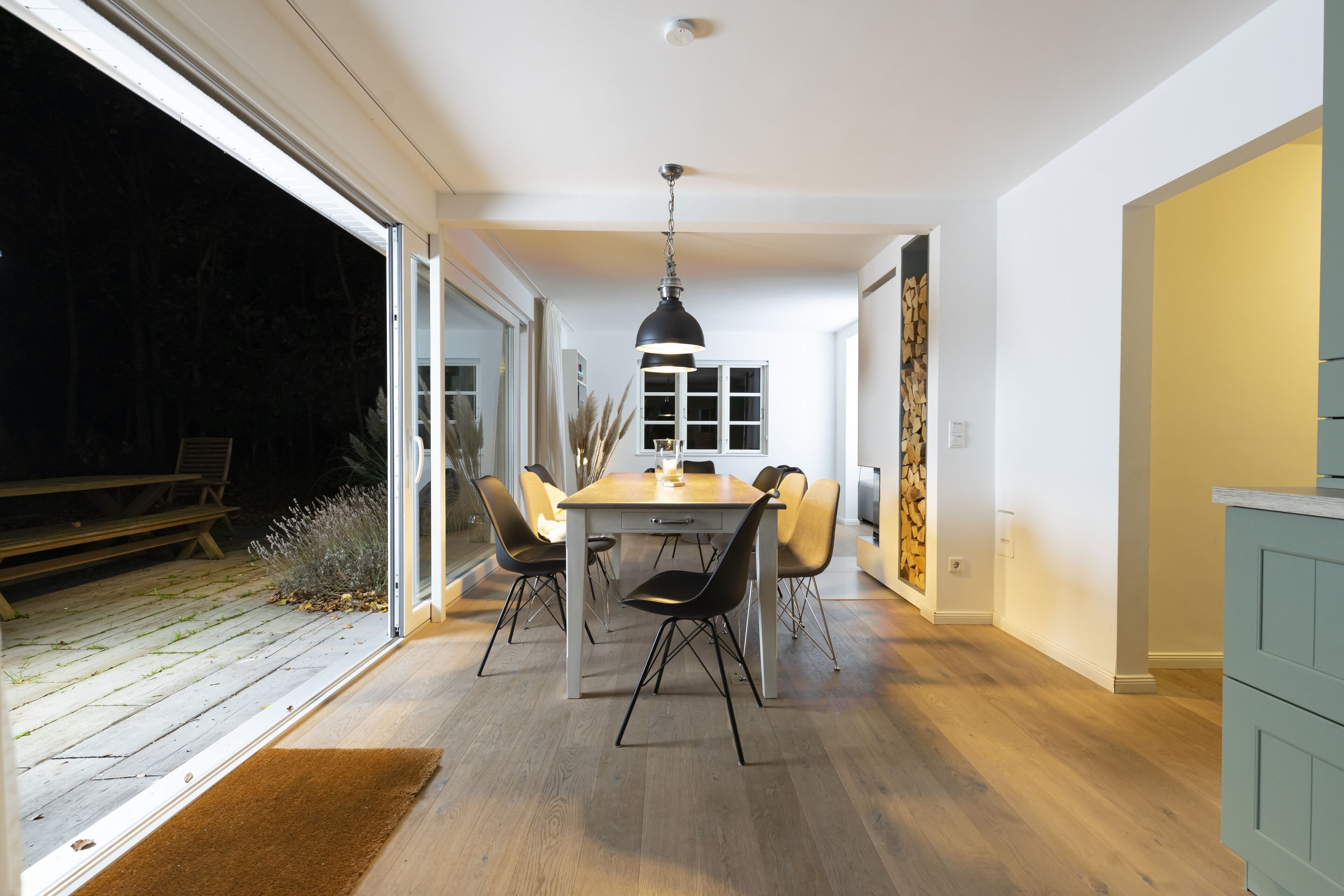 A modern dining area with a wooden table and chairs, a hanging light fixture, and a view of the outdoors.