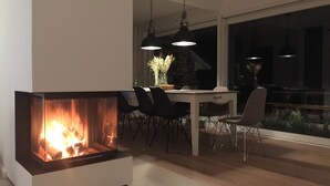 Un espace repas moderne doté d’une cheminée intégrée, d’une table à manger, de chaises et de luminaires suspendus.