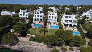 A coastal residential area with modern white buildings, clear blue pools, and a rocky shoreline.