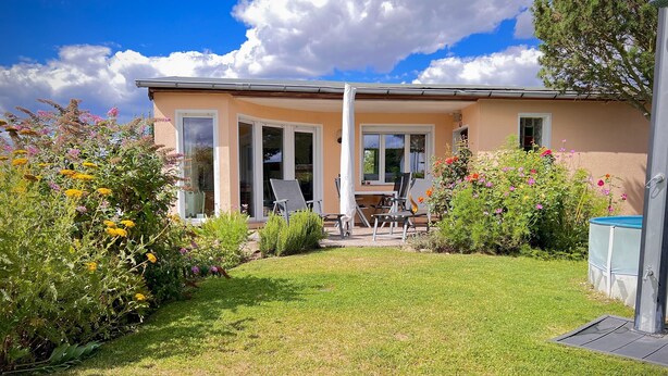 Une maison dotée d’un patio, d’une piscine et d’un jardin où poussent différentes plantes et fleurs.