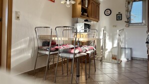 Un coin repas comprenant un buffet en bois, une table avec des chaises en métal et une fenêtre avec des stores.