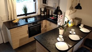 A modern kitchen with a central island, black countertops, wooden cabinets, and a window with curtains. - Great basement apartment in the middle of the island of Rügen in the outskirts of a village near mountains (Parchtitz)