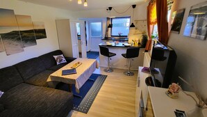 A compact living space with a sofa, a dining table, two chairs, a kitchen area, and artwork on the walls. - Great basement apartment in the middle of the island of Rügen in the outskirts of a village near mountains (Parchtitz)