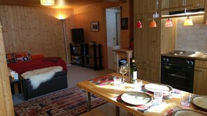 Una sala de estar acogedora con sofá, una mesa de centro y chimenea. Hay una zona de cocina con estufa, horno y mesa de comedor con platos y vasos.