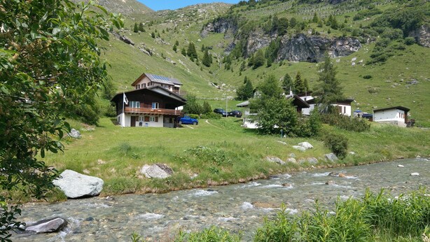 Una casa de montaña con fachada de madera, un balcón y un río en primer plano.