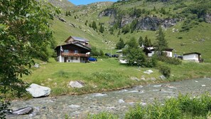 Una casa de montaña con fachada de madera, un balcón y un río al frente.