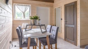 A cozy wooden room with a dining table and four chairs, a window with curtains, and a door. - Woodhouse Resort Dobrogoszcz (Dobrogoszcz)