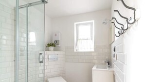 A modern bathroom with a glass shower enclosure, a small white pedestal sink, and a window with white curtains. - Woodhouse Resort Dobrogoszcz (Dobrogoszcz)
