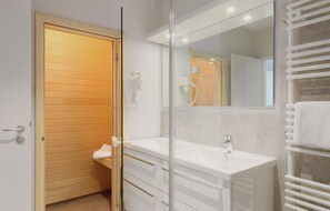 Een moderne badkamer met een houten deur, een douchecabine met glazen wanden, een witte wastafel en een handdoekhouder.