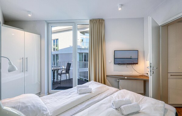 A hotel room with a bed, a desk, a chair, a TV, and a view of the outside balcony. - Dünenvilla 15, Whg 3 (Travemünde Waterfront)