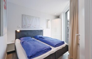 A modern bedroom with a bed, a headboard, a wall-mounted artwork, and a wardrobe. - Dünenvilla 15, Whg 3 (Travemünde Waterfront)