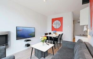 A modern living room with a flat-screen TV, a dining table with chairs, a grey sofa, and a red abstract painting on the wall. - Dünenvilla 15, Whg 3 (Travemünde Waterfront)