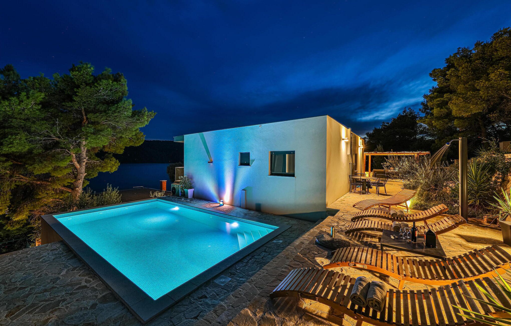 A modern outdoor pool area with a clear pool, lounge chairs, and a small building with windows.