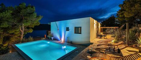 A modern outdoor pool area with a clear pool, lounge chairs, and a small building with windows.