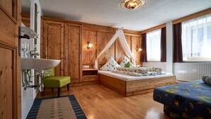 A wooden cabin-style bedroom with a bed, a green chair, a sink, and a window with curtains. - Beautiful, exclusively furnished apartment with 4 edelweiss  (Umhausen)