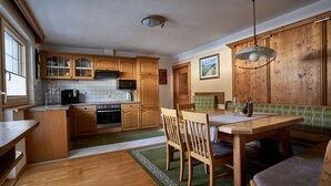 A kitchen with wooden cabinets, a dining table with chairs, a green rug, and a hanging light fixture. - Beautiful, exclusively furnished apartment with 4 edelweiss  (Umhausen)
