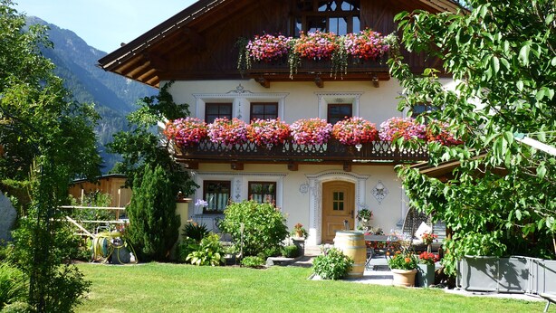 A traditional chalet with balconies adorned with flowers, a well-maintained garden, and a mountainous backdrop. - Beautiful, exclusively furnished apartment with 4 edelweiss  (Umhausen)