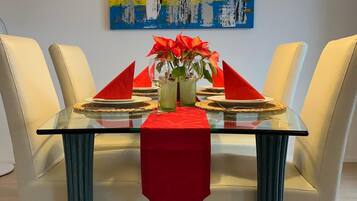 Ein Esstisch mit roter Tischdecke, zwei Glasvasen mit roten Blumen und ein farbenfrohes abstraktes Gemälde an der Wand.