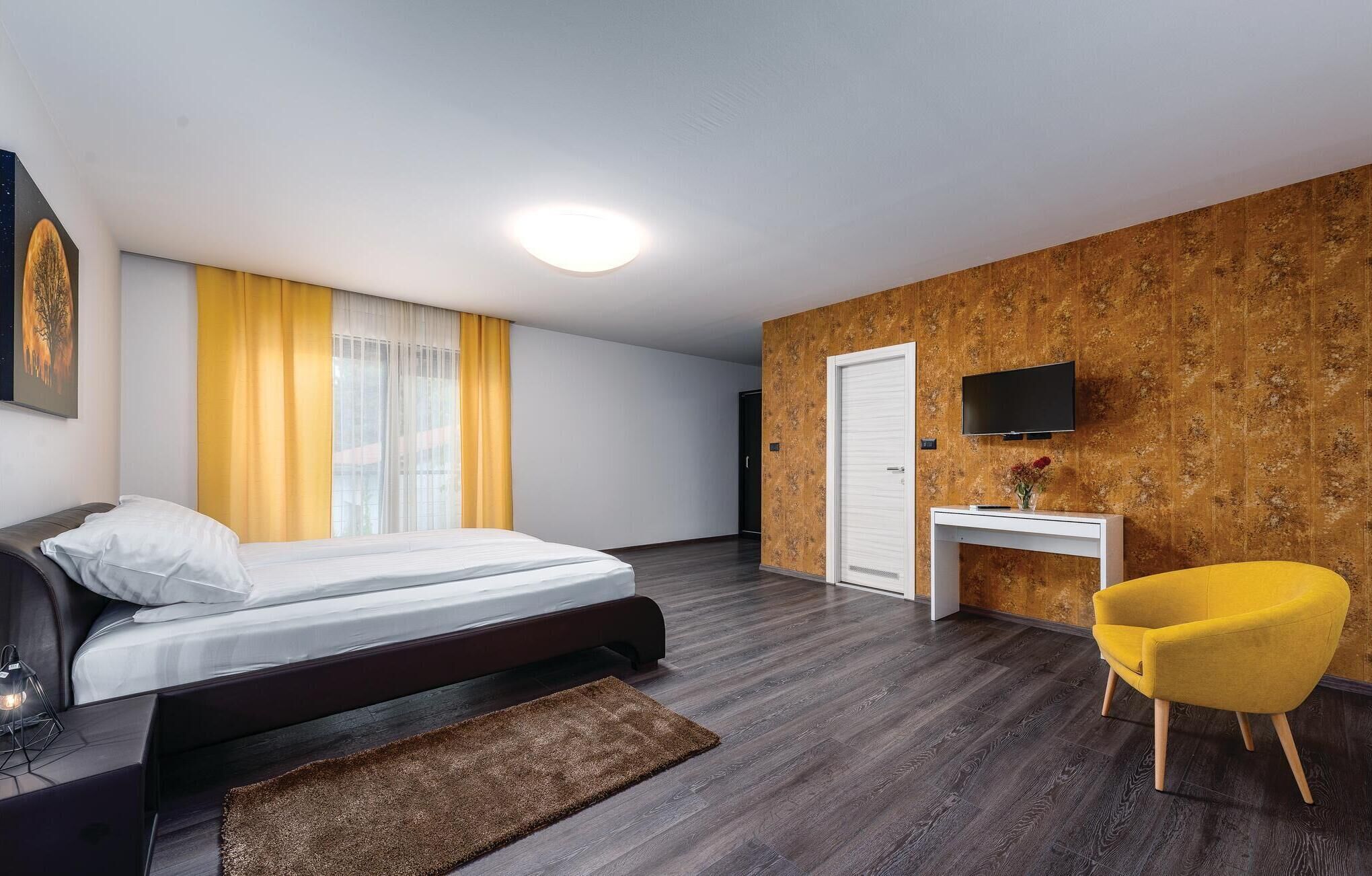 A hotel room with a bed, a desk, a chair, a TV, and a window with curtains.