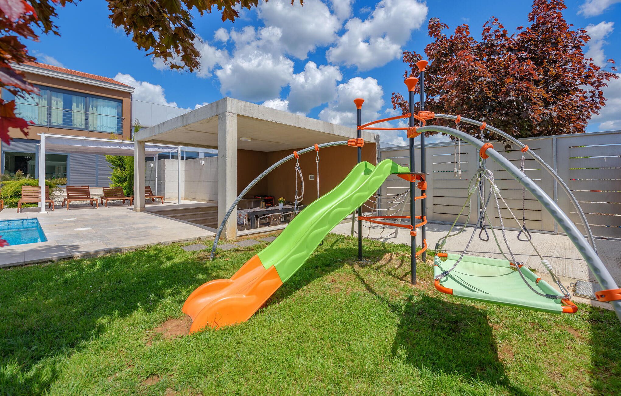 A playground with a slide and swings, a pool, and a covered patio area.