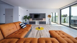 Ett modernt vardagsrum med en soffa, en tv, en växt och ett stort fönster.
