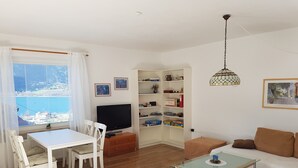 A living room with a TV, white furniture, a glass coffee table, and a view of the sea. - Holiday and relaxation on the Ossiacher See (Ostriach)