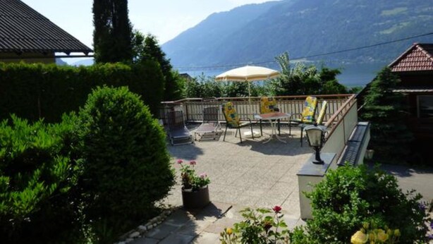 A patio with outdoor furniture, a table, and a chair, overlooking a lake and mountains. - Holiday and relaxation on the Ossiacher See (Ostriach)