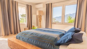 Een slaapkamer met een houten bed, uitzicht op bergen en een lamp.
