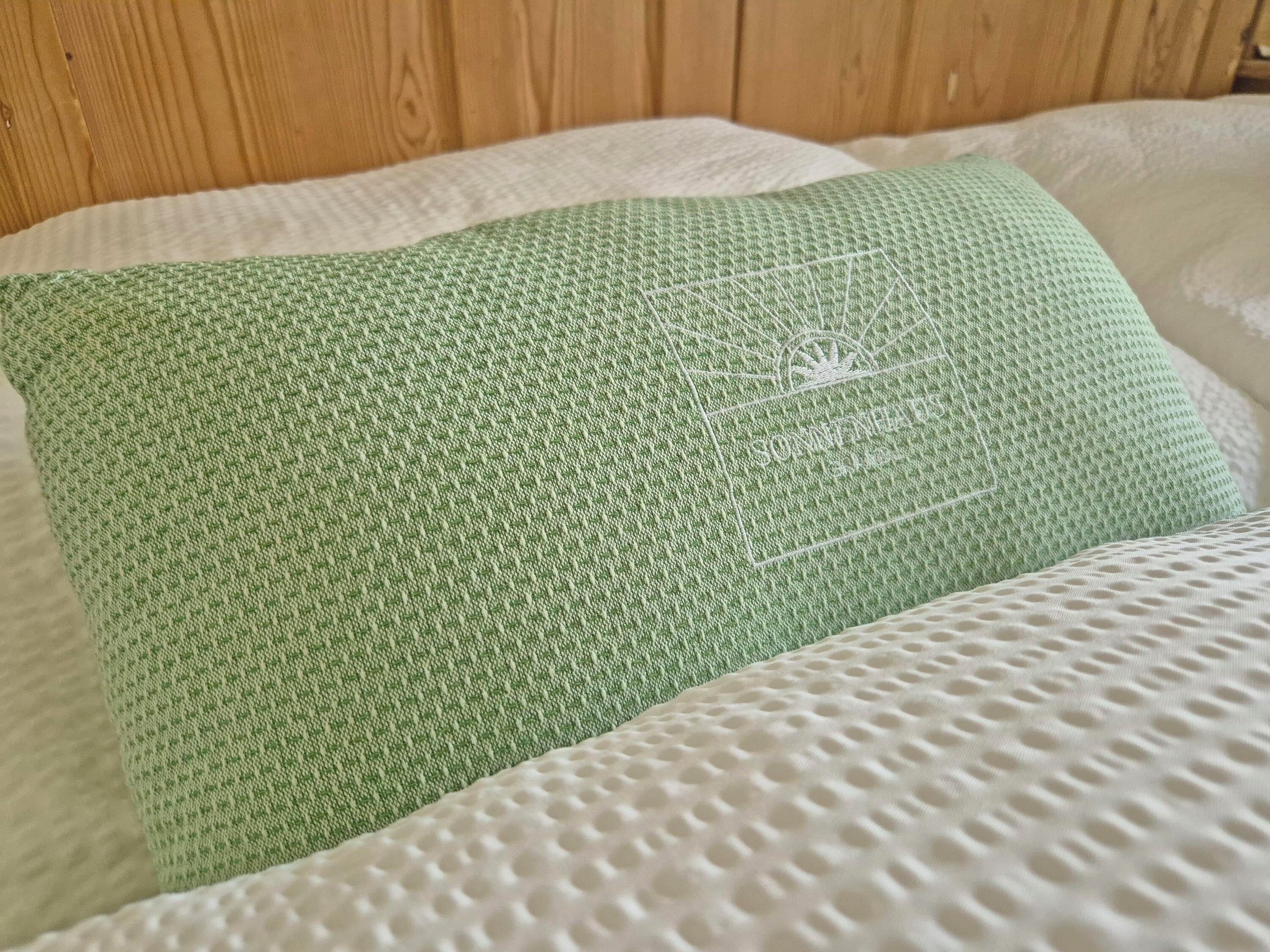 A bed with a green textured pillow and a white textured blanket.