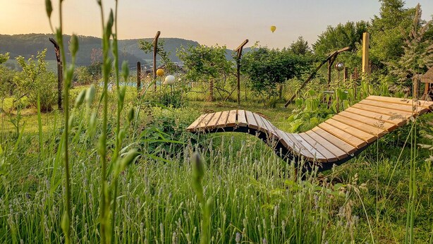 A wooden deck in a lush garden with a view of distant hills.