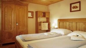 A bedroom with two beds, wooden wardrobe, and a small shelf with a lamp.