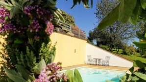 A swimming pool surrounded by lush greenery and a yellow building with outdoor seating.