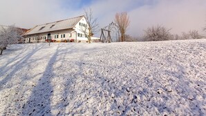 A snow-covered landscape with a house featuring a sloped roof and a chimney.