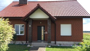Une maison en briques avec un toit recouvert de tuiles rouges, une porte d’entrée et un petit porche.